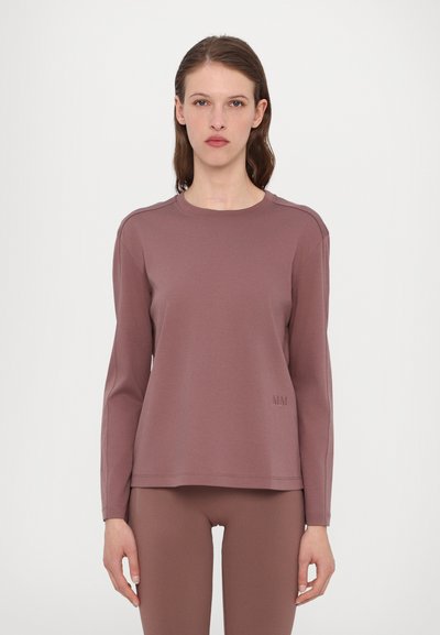 Sweatshirt mauve à manches longues avec un col rond, texture douce et broderie subtile "MM" sur l'ourlet. Associé à un pantalon assorti.