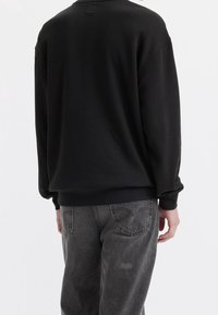 Felpa nera con colletto rotondo, spalle abbassate e polsini a costine, abbinata a jeans grigi sbiaditi con tasche posteriori.