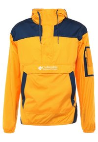 Chaqueta cortavientos amarilla y azul marino con medio cierre en la parte frontal, capucha ajustable y bolsillo de malla en la manga. Material suave y ligero.