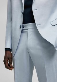 Hellblauer Anzug mit feiner Textur, der eine einreihige Jacke und maßgeschneiderte Hosen aufweist, akzentuiert durch dunkle Knöpfe und eine schwarze innere Schicht.