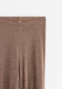 Brune leggings laget av et mykt, strukturelt stoff. Har et høyt liv og en jevn overflate uten mønstre eller synlig maskinvare.