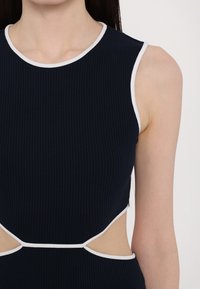 Laivaston sininen ribattua muotoilua oleva mekko, jossa on korkea kaulus, valkoiset yksityiskohdat ja aukot sivuilla. Sileä pinta ja istuva leikkaus.