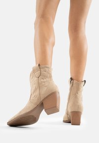 Botas de cowboy de ante color canela con diseño floral en relieve, caña de altura media, tacón en bloque en ángulo y cierre de cremallera en la parte trasera.