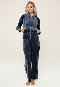 Ensemble de loungewear en velours bleu marine comprenant un hoodie zippé avec poches et un pantalon style cargo. Texture douce avec une coupe décontractée.