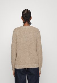 Beige stickad tröja med rund hals, med ett texturerat mönster. Långa ärmar och ribbade muddar. Matchad med mörka denimbyxor.