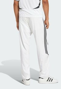 Vita sportbyxor med svarta sidostripes, med en lös passform och mjuk textur, kombinerade med svartvita sneakers.