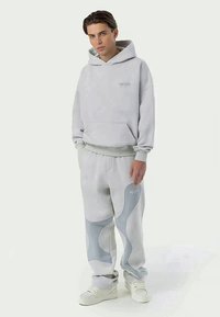 Grå hoodie med en rymlig framficka och en subtil logotyp, i kombination med matchande sweatpants som har ljusblå abstrakta mönster.