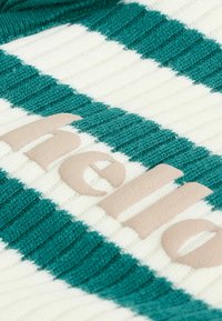 Knitted sweater with alternating teal and white stripes. Features plush beige lettering. Ribbed texture throughout the fabric.