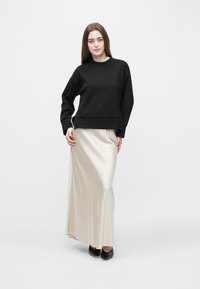 Black sweatshirt with a relaxed fit and long sleeves, paired with a cream satin maxi skirt. Black shoes complete the outfit.