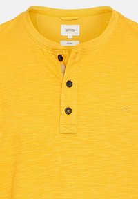Gul økologisk bomulds polo shirt med en delvis knaplukning med sorte knapper og en lille logo-detalje på brystet.
