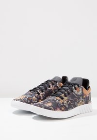 Les baskets à motif floral présentent une tige en tissu noir ornée de fleurs multicolores, un col rembourré gris et une semelle en caoutchouc blanche.