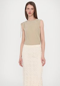 Top beige senza maniche con dettaglio di legatura sulle spalle, abbinato a una lunga gonna di crochet crema con motivi circolari. Tessuto morbido in tutta la superficie.