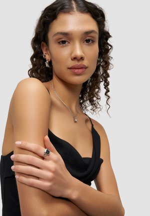 Silver jewelry includes a layered necklace with a geometric pendant, earrings with a similar design, and a ring with a square stone.