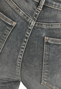 Vaqueros de denim gris con un diseño ajustado, bolsillos traseros con detalles de costura visibles y una textura ligeramente desgastada.