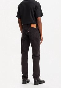 Jeans de mezclilla negros con corte recto, que cuentan con un parche de cuero en la parte trasera de la cintura y detalles de costura sutiles.