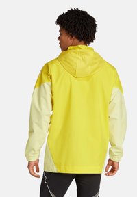 Veste imperméable jaune avec des accents jaune clair, capuche ajustable, poignets élastiques et coupe décontractée. Texture lisse et brillante.
