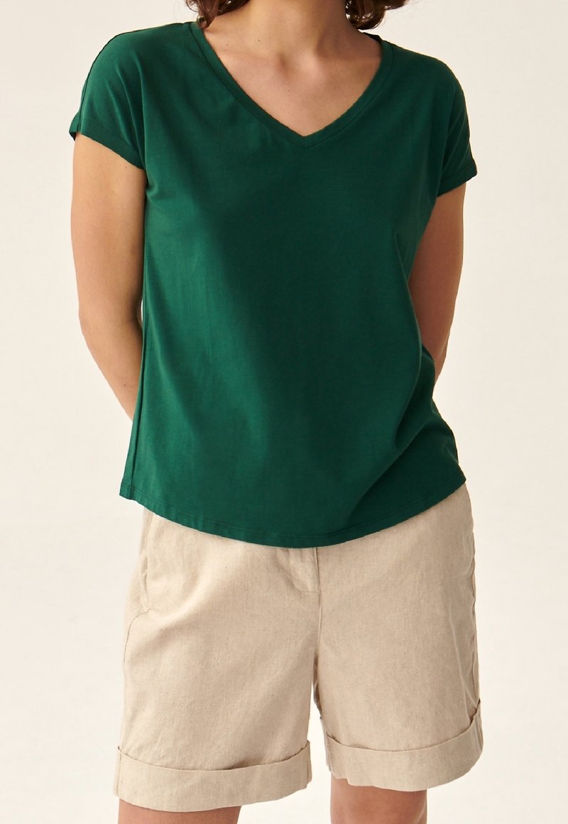 T-shirt verde a scollo a V realizzata in tessuto morbido, abbinata a pantaloni shorts beige chiaro con orlo arrotolato. L'outfit presenta una vestibilità rilassata e un design casual.