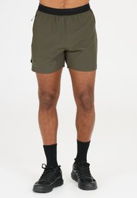 Olivgröna shorts med svart elastisk midjeband, lätt material och en subtil grön logotypdetalj på sidan. Shortsen når mitt på låret.