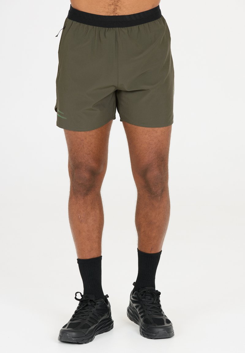 Olivgröna shorts med svart elastisk midjeband, lätt material och en subtil grön logotypdetalj på sidan. Shortsen når mitt på låret.