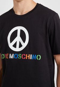 Zwart T-shirt van katoen, met een groot wit vredesteken en kleurrijke "LOVE MOSCHINO" tekst eronder in verschillende blokkleuren.