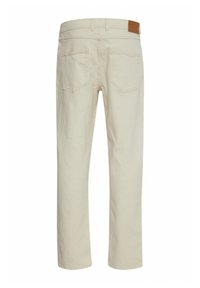 Pantalones beige de corte recto, fabricados en algodón. Presentan dos bolsillos traseros y un parche de cuero marrón en la cintura.
