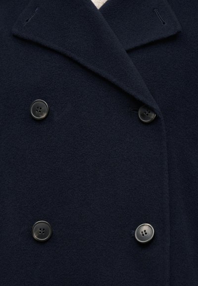Μακρύ μπλε ναυτικό παλτό από μαλλί με φαρδιά γιακά και τέσσερα μεγάλα μαύρα κουμπιά σε διπλή σειρά.