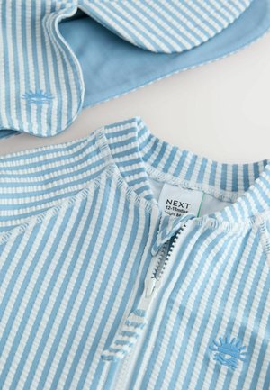 Detský overal svetlomodrej farby s pruhmi, vyrobený z mäkkej látky, s predným zipsom a vyšitým motívom slnka na hrudi.