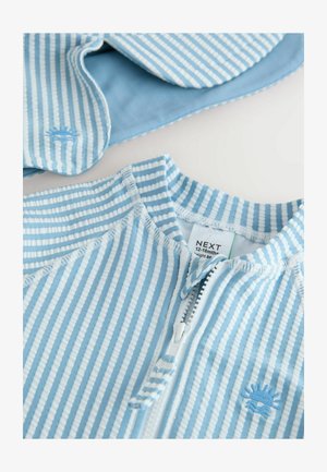 Hele sinine triibuline laste riietus, mis on valmistatud pehmest kangast, millel on esiküljel tõmblukk ja rinnal tikitud päiksemotiiv.