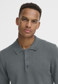 Grijze gebreide poloshirt met een klassieke kraag, drie donkere knopen en een gestructureerde stof met een aansluitende pasvorm.