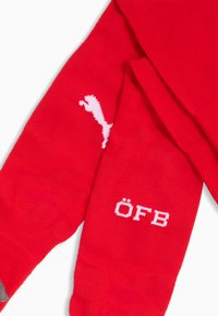 Calzini sportivi rossi in tessuto a maglia, con il logo Puma bianco e il testo "ÖFB" in bianco sul lato. Area testurizzata vicino alla caviglia.