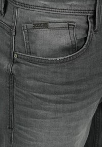 Gray denim jeans feature a classic design with a front pocket, a small brand tag, and metal hardware. The texture is smooth with subtle shading.