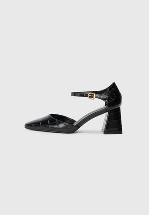 Black patent leather high-heeled shoe with pointed toe, ankle strap, and textured crocodile pattern. Square block heel design.