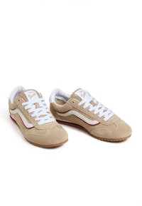 Zapatillas de ante en beige con acentos en cuero blanco, puntera redonda, cordones planos blancos y una suela de goma texturizada. Diseño retro con perforaciones.