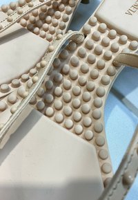 Sandale beige avec des brides et plusieurs clous ronds en caoutchouc couvrant la semelle pour l'adhérence et une sensation de massage.