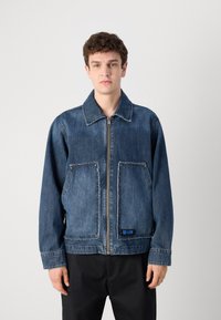 Jachetă din denim de culoare albastru deschis, cu fermoar în față, buzunare mari cu aplică, margini desfăcute și un etichetă de marcă la tiv. Mâneci lungi. Croială casual.