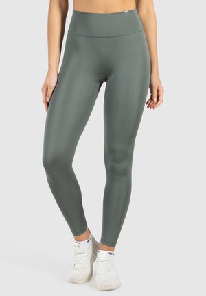 Hoch taillierte, grüne Sportleggings aus dehnbarem, glattem Stoff. Eng anliegendes Design, nahtlose Konstruktion, kombiniert mit weißen Sportschuhen.