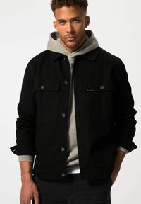 Zwarte jas met twee borstzakken, knoopsluiting en een grijze hoodie eronder. Gladde textuur en moderne silhouet.