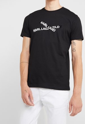 T-shirt en coton noir avec un texte blanc superposé "KARL LAGFELD" et "KARL LAGIE !" en police sans serif audacieuse. Col rond.