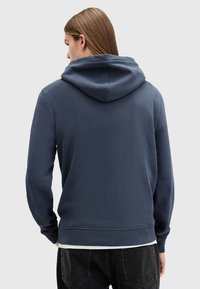 Navy blue hoodie with a large hood, soft texture, ribbed hem and cuffs, worn over a white shirt, showing a casual design.