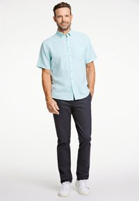 Jasnoniebieska koszula zapinana na guziki z krótkim rękawem i kieszenią na piersi, noszona z ciemnogranatowymi spodniami i białymi trampkami. Gładka tekstura tkaniny.