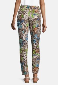 Beige broek met bloem- en luipaardprint, voorzien van groene, blauwe en oranje accenten. Elastische tailleband en taps toelopende pijpen met een soepele textuur.