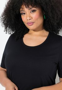 Černé tričko s krátkým rukávem a kulatým výstřihem vyrobené z měkkého materiálu. Tkanina má hladký povrch a pohodlně se nosí.