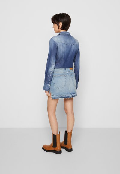 Jaqueta de ganga com um degradê azul claro, combinada com uma saia de ganga azul clara desfiada e botas Chelsea castanhas com painéis elásticos pretos.