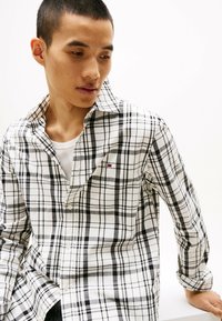 Black and white plaid button-up shirt with a slim fit, featuring a chest logo and a soft cotton fabric. Long sleeves and collar design.