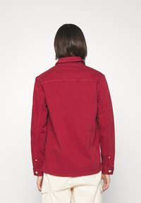 Veste en coton rouge avec un col, des poignets boutonnés et un design uni, vue de dos sur fond blanc.