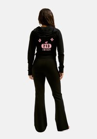 Zwarte trainingsset met een hoodie met roze graphics, label "213 JUICY", en uitlopende broek. Materiaal lijkt zacht en rekbaar.