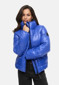 Puffer jacket in glossy royal blue, featuring a high collar, zip closure, and quilted design. Black accent label on left shoulder.
