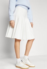White pleated skirt with a high waistband, paired with white sneakers and knee-high socks. Soft texture, structured design. Casual look.