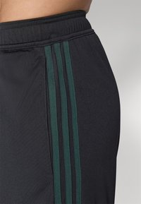 Sorte atletiske shorts lavet af blødt materiale, med grønne striber langs siden, en elastisk talje og en glat tekstur.