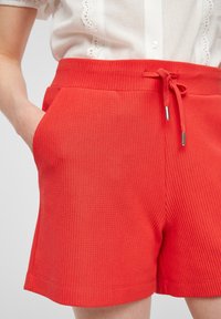 Rode geribbelde shorts met een elastische tailleband en een trekkoord, twee zijzakken en een gladde textuur.